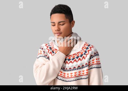 Kranker afroamerikanischer Typ mit Halsschmerzen auf grauem Hintergrund Stockfoto