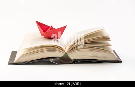 Origami rotes Papierboot auf einem Buch. Nahaufnahme Makrofotografie. Konzept von Reisen und Forschung - Wissen Stockfoto