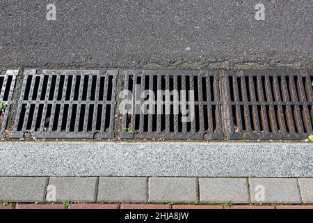 Fangen Becken Gitter des Gitters des Abflusssystems für die Ableitung von Regenwasser von der Straßenoberfläche mit einer asphaltierten Straße an Granit Bordstein mit einem Stein t Stockfoto