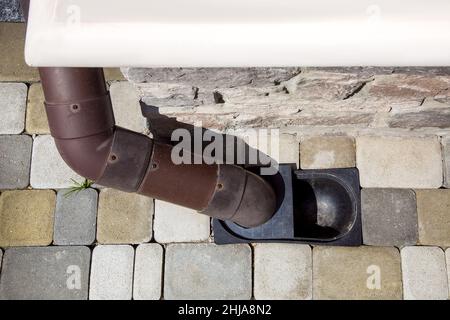 Fallrohr aus braunem pvc-Kunststoff, das Regenwasser vom Dach des Hauses in das Bodenentwässerungssystem an der Ecke der Fassade des mit Nat ausgekleideten Gebäudes ableiten lässt Stockfoto