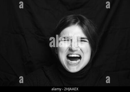 Junge Frau schreit, hasst, Wut. Weinende emotionale wütende Frau, die auf schwarzem Hintergrund schreit. Emotionales, junges weibliches Gesichtsausdruckkonzept. Blac Stockfoto