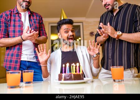 Aufgeregt arabischen Mann bereit, Kerzen auf Kuchen auf Geburtstagsfeier mit glücklichen Freunden im Haus zu blasen Stockfoto