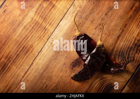 Chile Guajillo. Diese mexikanische Chili ist die getrocknete Form von mirasol Chili und wird in einer Vielzahl von mexikanischen Zubereitungen verwendet. Rustikales Holzbrett. Flach liegend Stockfoto