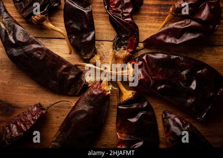 Chile Guajillo. Diese mexikanische Chili ist die getrocknete Form von mirasol Chili und wird in einer Vielzahl von mexikanischen Zubereitungen verwendet. Rustikales Holzbrett. Nahaufnahme Stockfoto