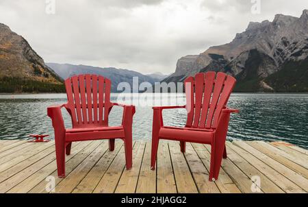 Zwei leuchtend rote Adirondack-Stühle im Banff National Park, Kanada. Zwei rote komfortable Liegestühle am See Stockfoto