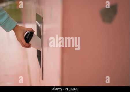 Eine Frau wirft eine Tasse Kaffee in einen Mülltonnen in der Wand eines Cafés. Stockfoto