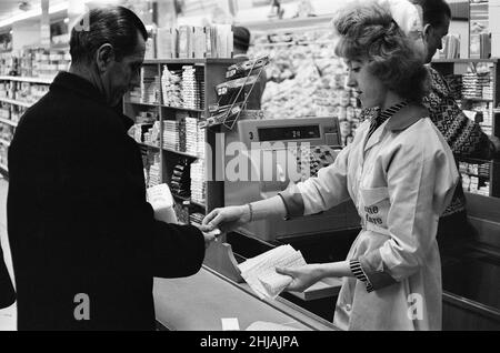 Shopper, Fine Fare Supermarket, Wilton, London, 29th. Oktober 1963. Sammeln Sie Green Shield Briefmarken an der Kasse, nachdem Sie für Waren bezahlt haben. Green Shield Stamps ist ein britisches Verkaufsförderungsprogramm, das Käufer mit Briefmarken belohnt, die eingelöst werden können und zum Kauf von Geschenken aus einem Katalog oder einem angeschlossenen Einzelhändler verwendet werden. Stockfoto