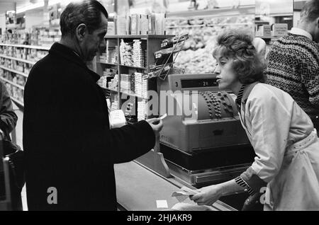 Shopper, Fine Fare Supermarket, Wilton, London, 29th. Oktober 1963. Sammeln Sie Green Shield Briefmarken an der Kasse, nachdem Sie für Waren bezahlt haben. Green Shield Stamps ist ein britisches Verkaufsförderungsprogramm, das Käufer mit Briefmarken belohnt, die eingelöst werden können und zum Kauf von Geschenken aus einem Katalog oder einem angeschlossenen Einzelhändler verwendet werden. Stockfoto