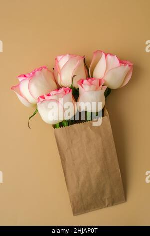 Zarte rosafarbene Rosen in einer Bastelpapiertasche auf beigem Hintergrund. Minimalistisch trendige Komposition. Abstrakte Kunstidee. Romantische rosa Rosenblüten in Pastelltönen. Moderne Ästhetik. Neutrale Erdtöne. Grußkarte Hintergrund Kopierbereich Banner Stockfoto