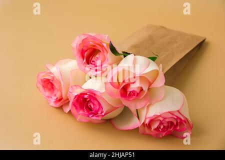Zarte rosafarbene Rosen in einer Bastelpapiertasche auf beigem Hintergrund. Minimalistisch trendige Komposition. Abstrakte Kunstidee. Romantische rosa Rosenblüten in Pastelltönen. Moderne Ästhetik. Neutrale Erdtöne. Grußkarte Hintergrund Kopierbereich Banner Stockfoto