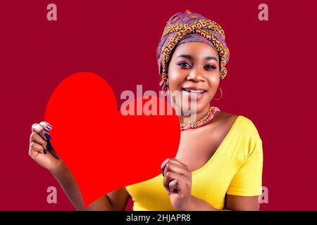 Attraktive schöne Frau aus dem Süden mit Turban hält in den Händen Herz isoliert über rotem Hintergrund valentinstag 14. februar Stockfoto