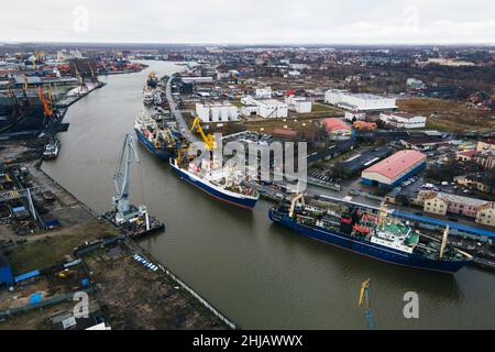 Ein großes blaues Schiff und gelbe Kraniche auf dem Wasser im Hafen einer Industriestadt. Frachttransport auf dem Seeweg. Konzept. Draufsicht, Luftaufnahme Stockfoto