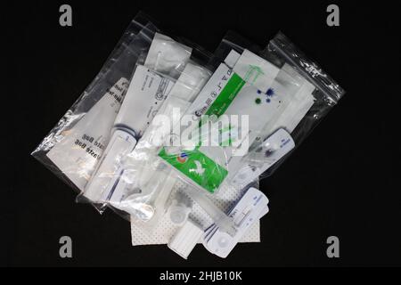 Stapel von gebrauchten negativen COVID-19-Seitenströmungstests in Kunststoffbeuteln mit Kunststofftupfer und Extraktionsröhrchen auf schwarzem Hintergrund Stockfoto
