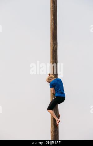 GOMEL, WEISSRUSSLAND - 21. Februar 2014: Junge Frau klettert auf einem Holzpfosten auf traditionellen Feiertag, der dem Herannahen des Frühlings gewidmet ist - slawisch Stockfoto