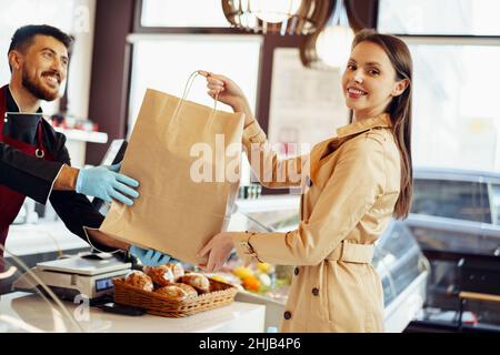 Verkäuferin, die Einkaufstasche an weibliche Kundin im Lebensmittelgeschäft abgibt Stockfoto