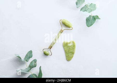 Gesicht Jade Walze, gua Sha, Eukalyptus Zweige auf Steinoberfläche. Flach liegend, Draufsicht, Overhead. Stockfoto