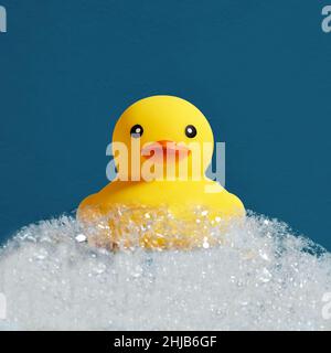 Gelbes Entenspielzeug aus Gummi schwimmt auf Seife oder Shampoo-Schaumstoff in der Badewanne. Badewanne mit Seifenschaum, zum Entchen in Schaumbad.