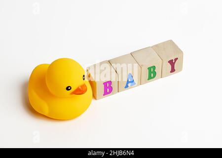 Das Wort Baby mit bunten Buchstaben auf Holzblöcken mit einer Spielzeug-Gummiente auf weißem Hintergrund geschrieben. Stockfoto