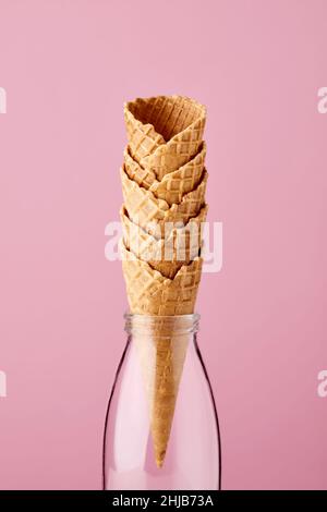Leere Eiszapfen in Glasmilchflasche auf pastellrosa Hintergrund. Stockfoto