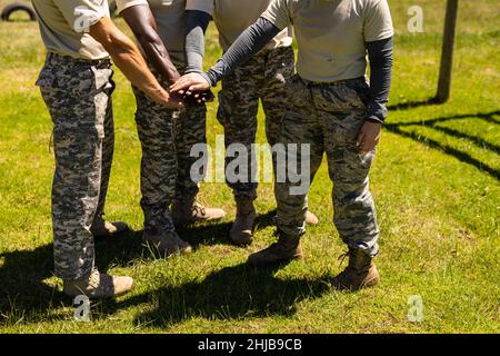 In der Mitte der Gruppe verschiedener männlicher und weiblicher Soldaten stapeln sich die Hände im Bootcamp zusammen Stockfoto