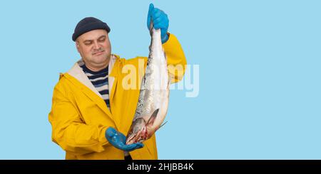 Fischer im gelben Anzug hält einen frisch gefangenen Fisch in den Händen. Fänger im Regenmantel. . Stockfoto