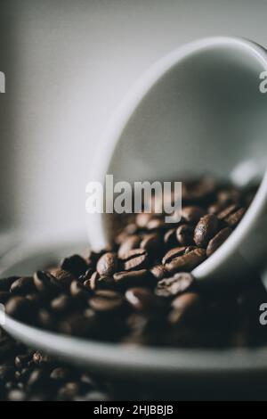Eine vertikale Aufnahme einer vollen Tasse frisch gerösteter Kaffeebohnen auf einer Untertasse auf dem Tisch Stockfoto