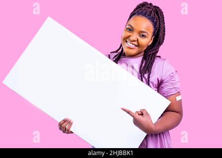 Positive Frau bekommt eine Impfung und hält ein weißes leeres Poster in der Hand mit Gips in einem rosa Studio-Kopierraum Stockfoto