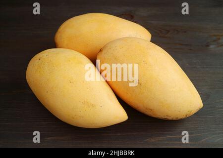 Drei frische reife Mango-Vollfrüchte isoliert auf schwarzem Holzhintergrund Stockfoto