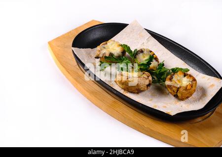 Gebackene gefüllte Pilze mit Pilzen, Käse und Kräutern, auf einem Holzbrett auf einem weißen isolierten Hintergrund. Stockfoto