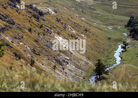 Wunderschöne natürliche Schlucht mit Hügeln, Gras und Bäumen. Am Ende der Schlucht fließt ein Fluss. Atemberaubende Landschaft für den Tourismus Stockfoto