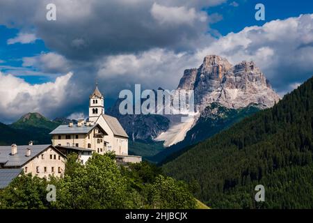 Die Kirche Chiesa Santa Lucia in Colle Santa Lucia am Fuße des Giau-Passes, Passo di Giau, der Gipfel des Monte Pelmo in der Ferne. Stockfoto