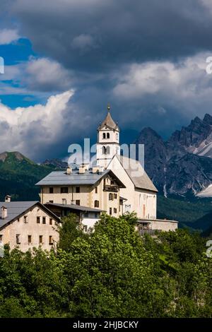 Die Kirche Chiesa Santa Lucia in Colle Santa Lucia am Fuße des Giau-Passes, Passo di Giau, der Gipfel des Monte Pelmo in der Ferne. Stockfoto