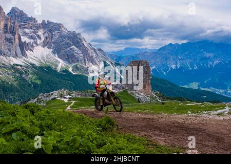 Ein Mann, der mit einem Cross-Motorrad auf die Berghütte Refugio Averau, das Rifugio Scoiattoli und Cinque Torri unten fährt, Tofana-Gruppe in der Ferne. Stockfoto