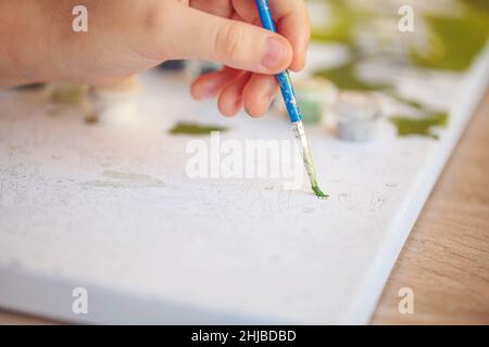 Verschwommenes beschnittenes Foto von weiblicher Handmalerei mit Pinsel auf Papier, selektiver Fokus auf Acrylfarben in Kunststoffkisten, die nach Shad in Reihe angeordnet sind Stockfoto