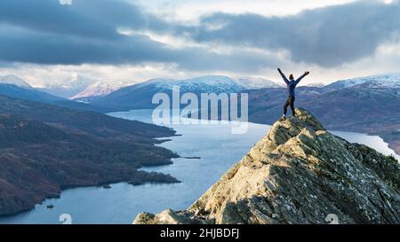 Weibliche Wandererin auf dem Gipfel von Ben A'an im Winter mit Blick auf Loch Katrine, Loch Lomond und den Trossachs National Park, Schottland, Großbritannien Stockfoto