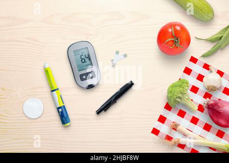 Blutzuckermessgerät und Insulininspritze auf dem Tisch neben gesunden Lebensmitteln - Gemüse. Draufsicht, flache Lay-Komposition Stockfoto