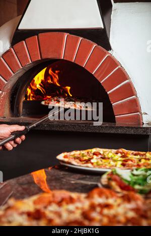 Der Koch nimmt Pizza. Italienische Pizza wird in einem Holzofen zubereitet Stockfoto