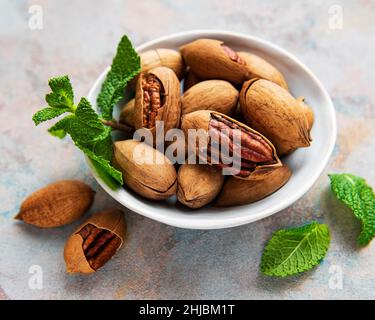 Pekannüsse in Schale auf grauem Betongrund Stockfoto