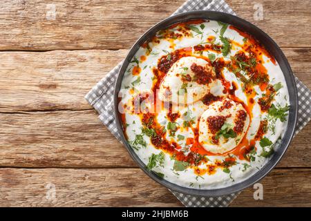 Cilbir ist ein türkisches Ei, das garlicky Joghurt, pochierte Eier und gewürzte geschmolzene Butter auf dem Teller auf dem Holztisch enthält. Horizontale Ansicht von oben Stockfoto