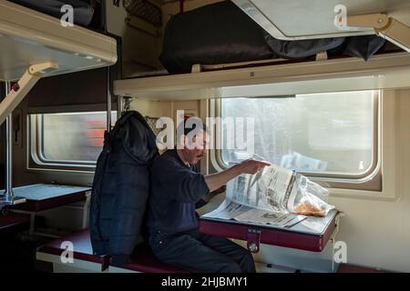 Tägliches Leben im Transsibirischen Express. Der Passagier liest Zeitung in der Plastkart-Sektion. Stockfoto