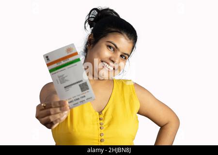 Eine junge indische Frau, die mit einer Aadhaar-Karte in der Hand auf weißem Hintergrund lächelt Stockfoto