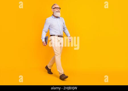 Foto von glücklichen niedlichen reifen Mann gekleidet formalen Outfit Brille halten Gadget zu Fuß leeren Raum isoliert gelben Hintergrund Stockfoto
