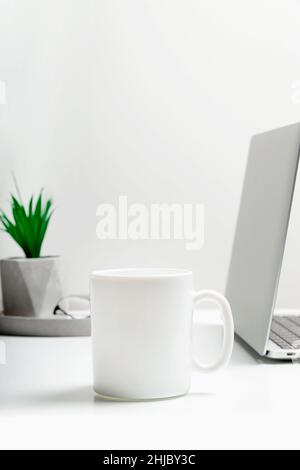 Weißer Becher-Mockup auf einem modernen, stilvollen Arbeitsplatz mit Laptop. Cup-Mockup. Stockfoto