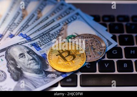 Bitcoin auf einer Laptop-Tastatur und 100-Dollar-Scheine in blauem Licht. Zahlung in Kryptowährung im Metaverse. Selektiver Fokus Stockfoto