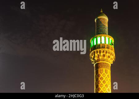 Beleuchtetes Minarett der iranischen Moschee (Imam Hussein Moschee) in Dubai, farbenfrohe Fassade aus persischen Fliesen mit orangefarbenen, gelben Steinen. Stockfoto