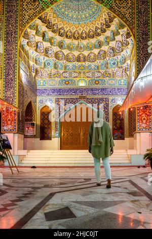 Muslimische Frau, die die iranische Moschee (Imam Hussein Moschee) in Dubai mit farbenfroher Fliesenfassade und persischer Architektur betreten hat. Stockfoto