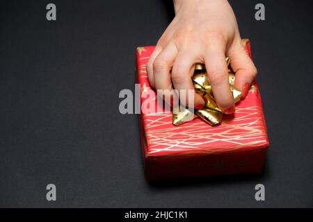 Eine Frauenhand greift an einer Schleife auf schwarzem Hintergrund zu einer Geschenkbox mit einem Platz für Text. Stockfoto