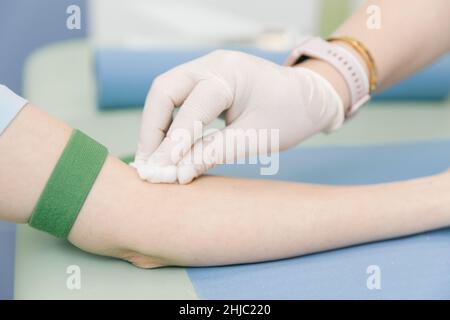 Durchführung eines Bluttests an einer Vene im Behandlungsraum. Die Krankenschwester stitzt eine Spritze mit einer Nadel in die Hand des Patienten. Der Tupfer wird gegen den gedrückt Stockfoto