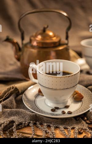 Zwei Tassen Kaffee, eine kupferne Teekane im Hintergrund, Braun- und Grautöne, Stoff in Grautönen Stockfoto