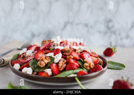 Teller mit hausgemachtem frischen Salat mit Babyspinatblättern, in Scheiben geschnittenen Erdbeeren, Walnüssen, Feta-Käse und einem leichten Vinaigrette-Dressing. Stockfoto